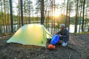 Mies teltassa auringonlaskuna ikaan