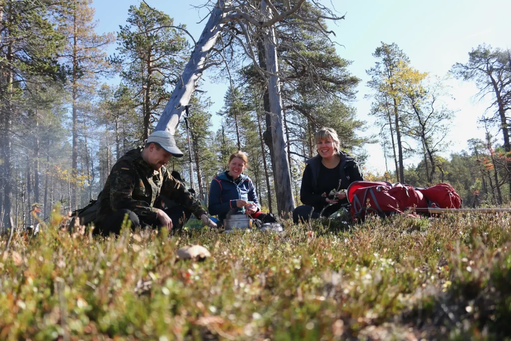 Ihmiset istuvat rivissä metsässä Lemmenjoen kansallispuistossa