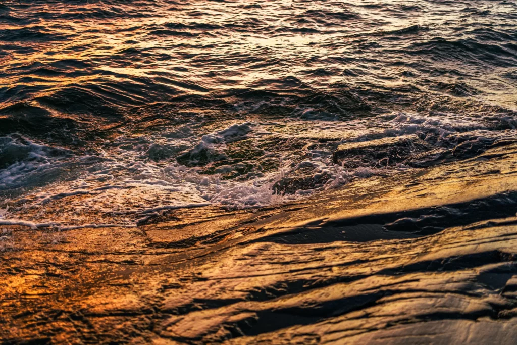 Ilta-aurinko heijastuu meren aalloista, kun ne lyövät rantakallioihin