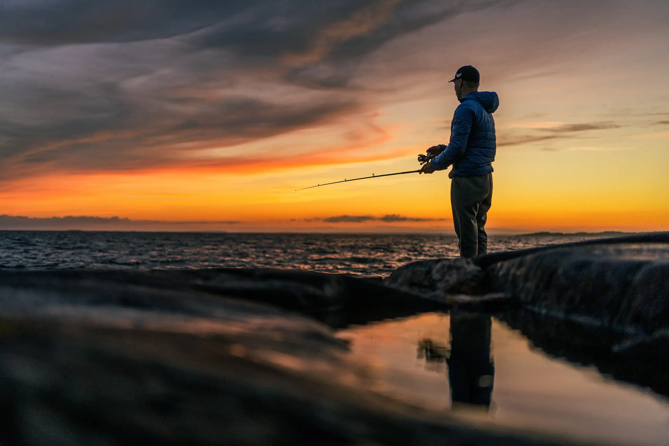 Mies kalastaa auringonlaskun aikaan