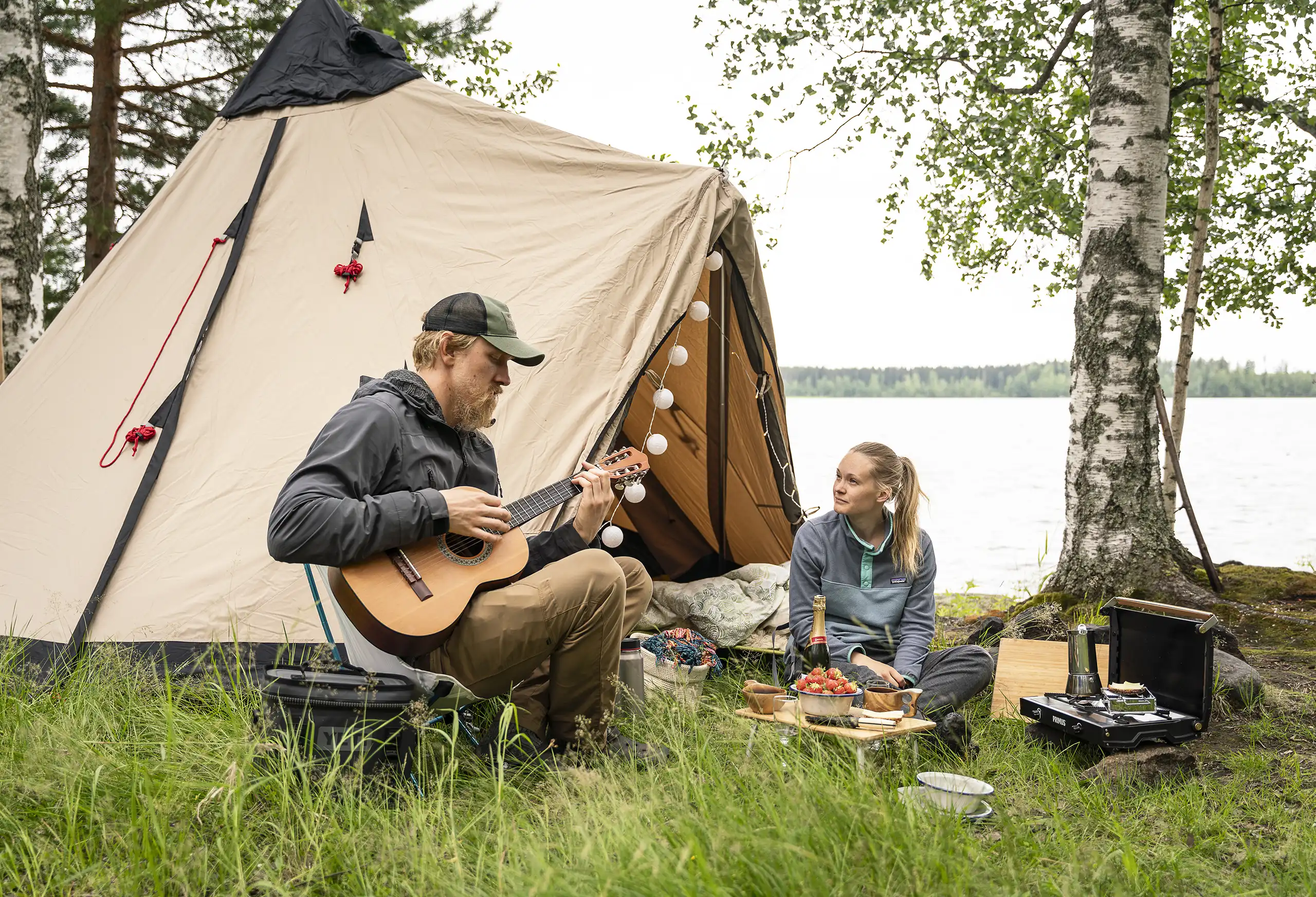 Mies soittaa kitaraa ja nainen istuu glamping-teltan edessä
