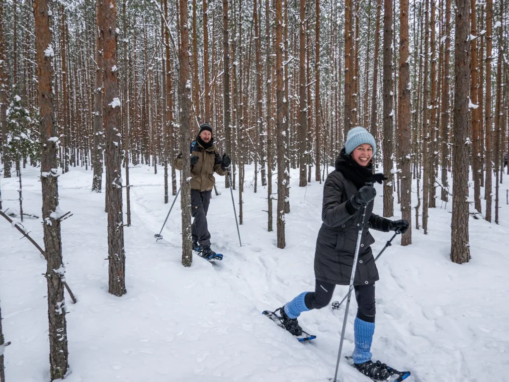 Mies ja nainen lumikenkäilevät lumisessa metsässä